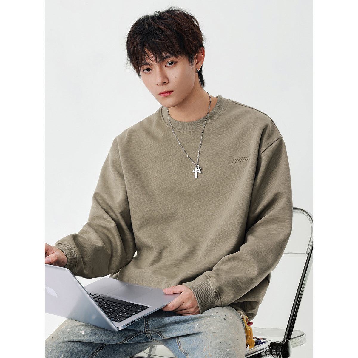 Model wearing an oversized taupe crewneck sweatshirt with ribbed trim and a small embroidered chest logo.