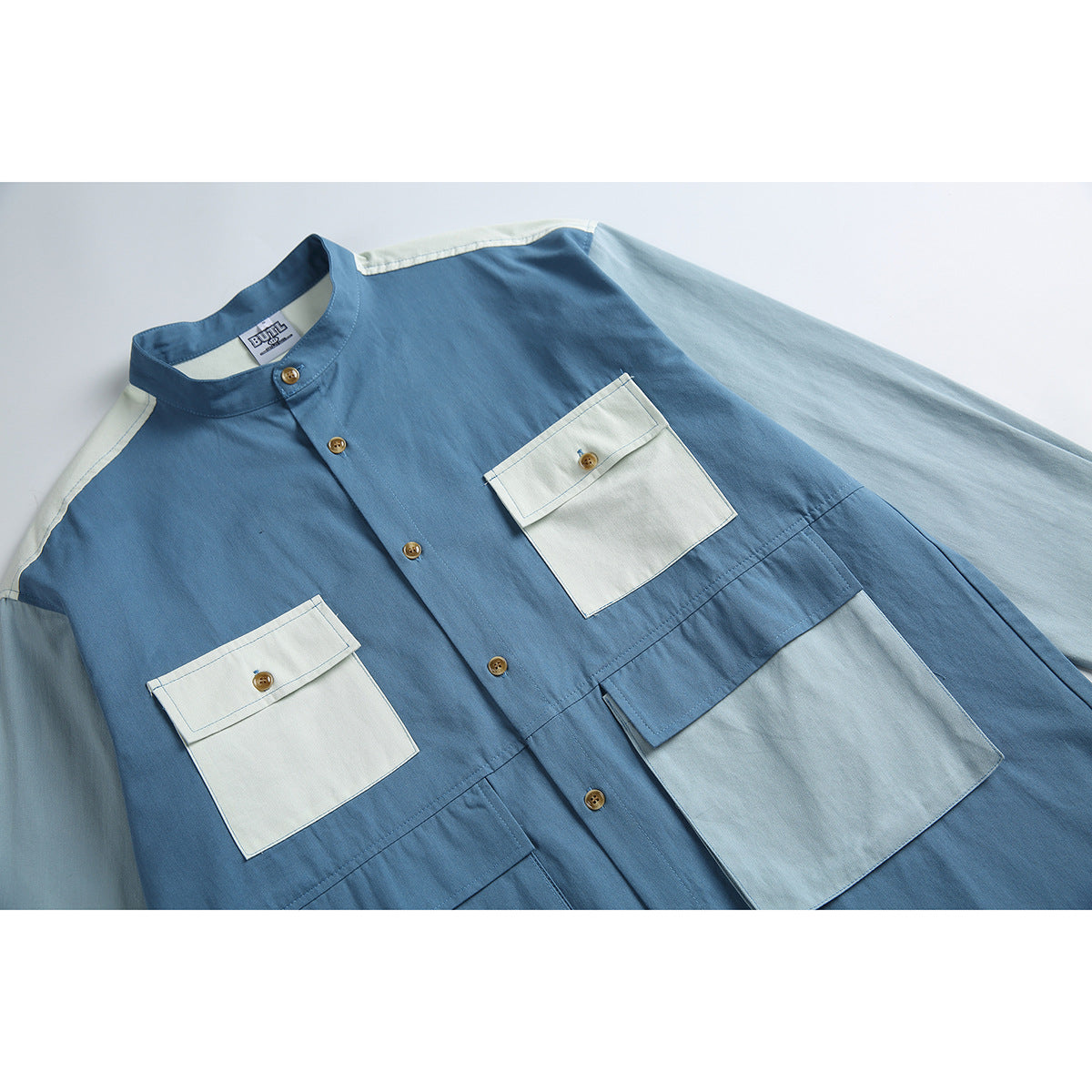 Close view of a blue and pale blue color-block shirt with a band collar, brown buttons, and four flap pockets.