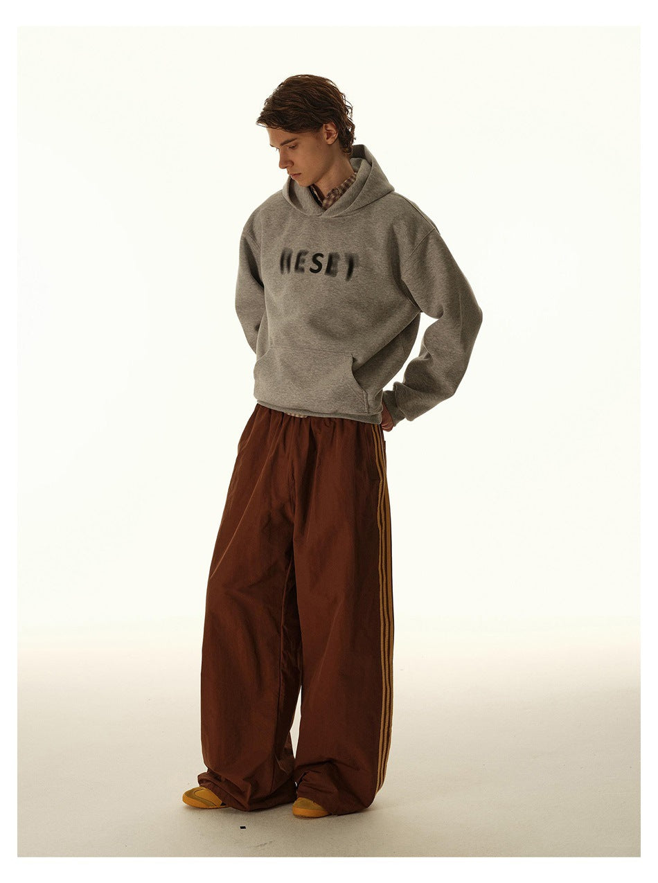 Model wearing brown wide-leg pants with tan side stripes, a gray hoodie and yellow shoes