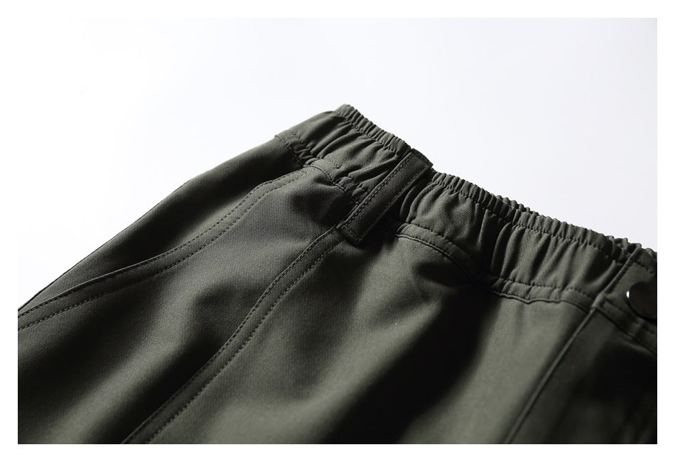 Close-up of the elastic waistband, belt loop, and front pocket on dark olive pants.