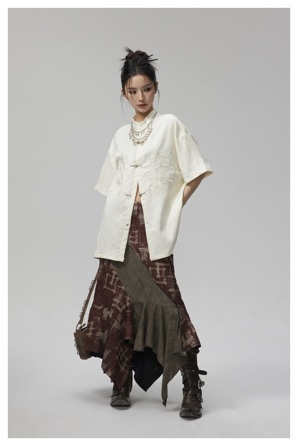 Model in the beige short-sleeve shirt with embroidered bamboo leaves and metal fasteners, styled with a skirt and boots