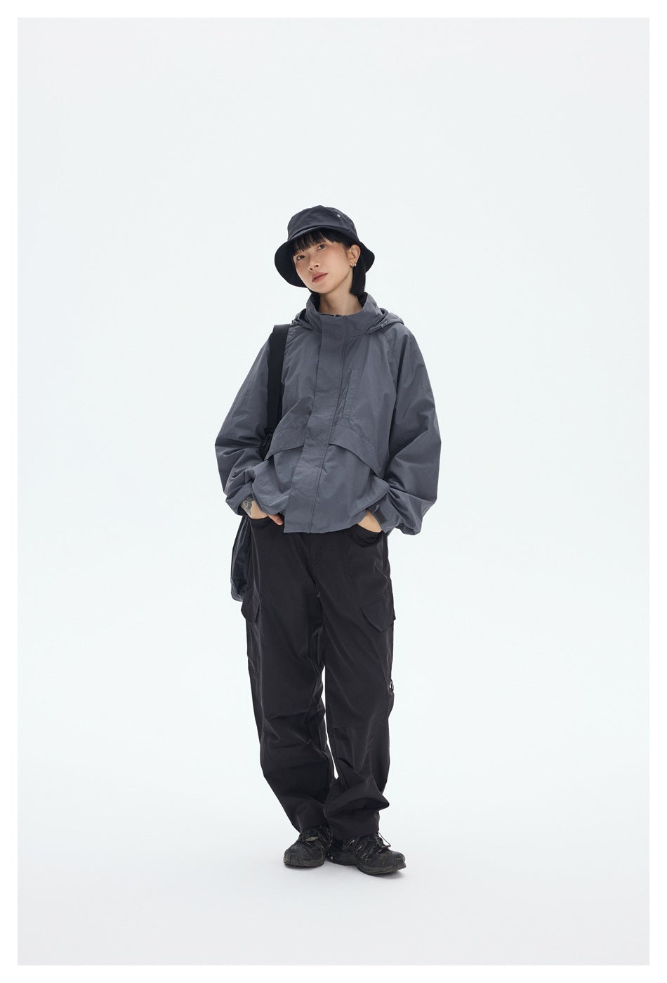 Model wearing a gray hooded jacket and black cargo pants with a black bucket hat and shoulder bag.