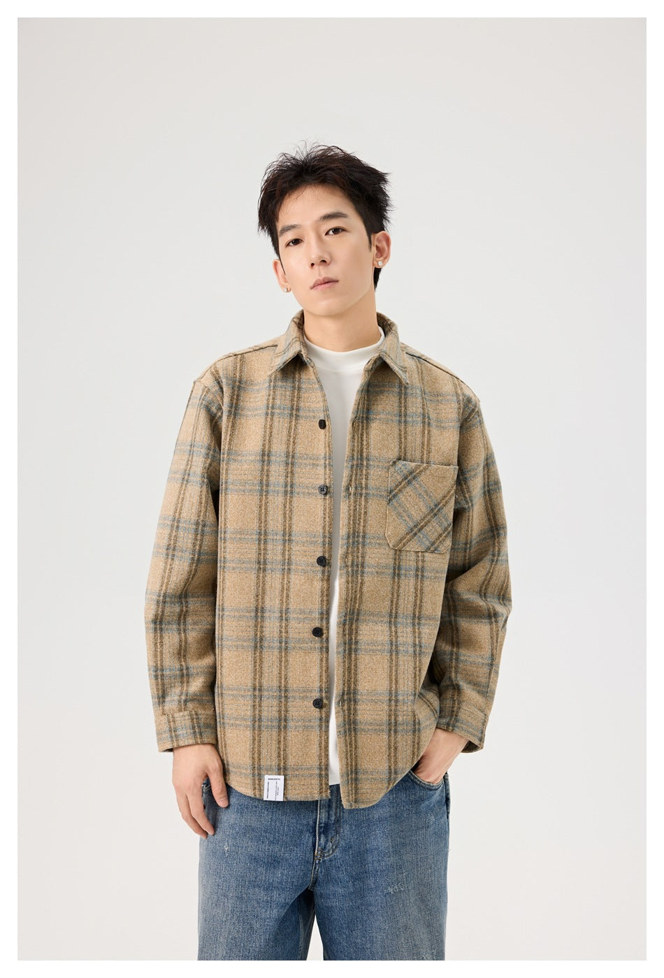 A man wears a tan plaid button-front overshirt with a single chest pocket, shown from head to hips.