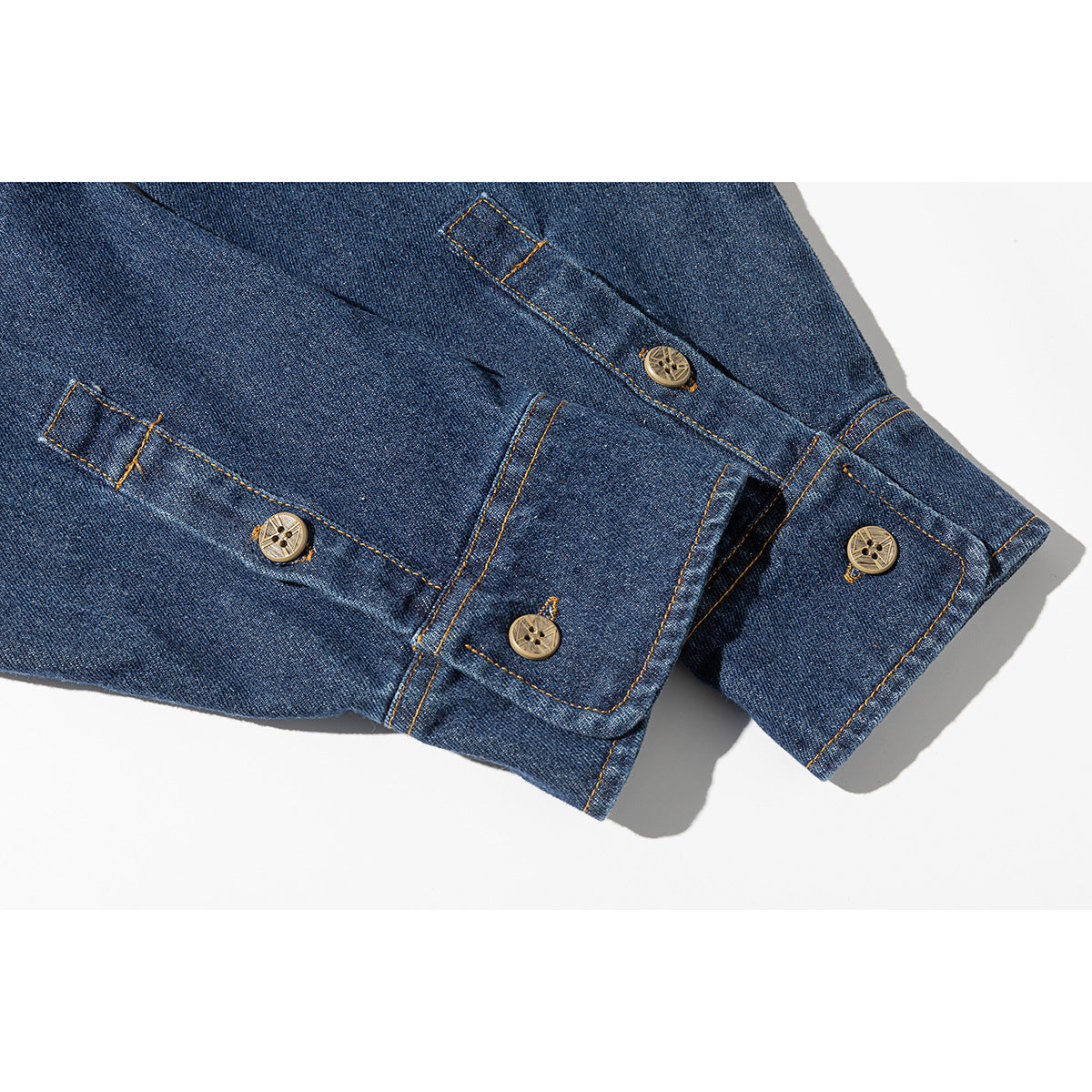 Close-up of a dark blue denim shirt sleeve cuff with tan buttons and orange stitching.