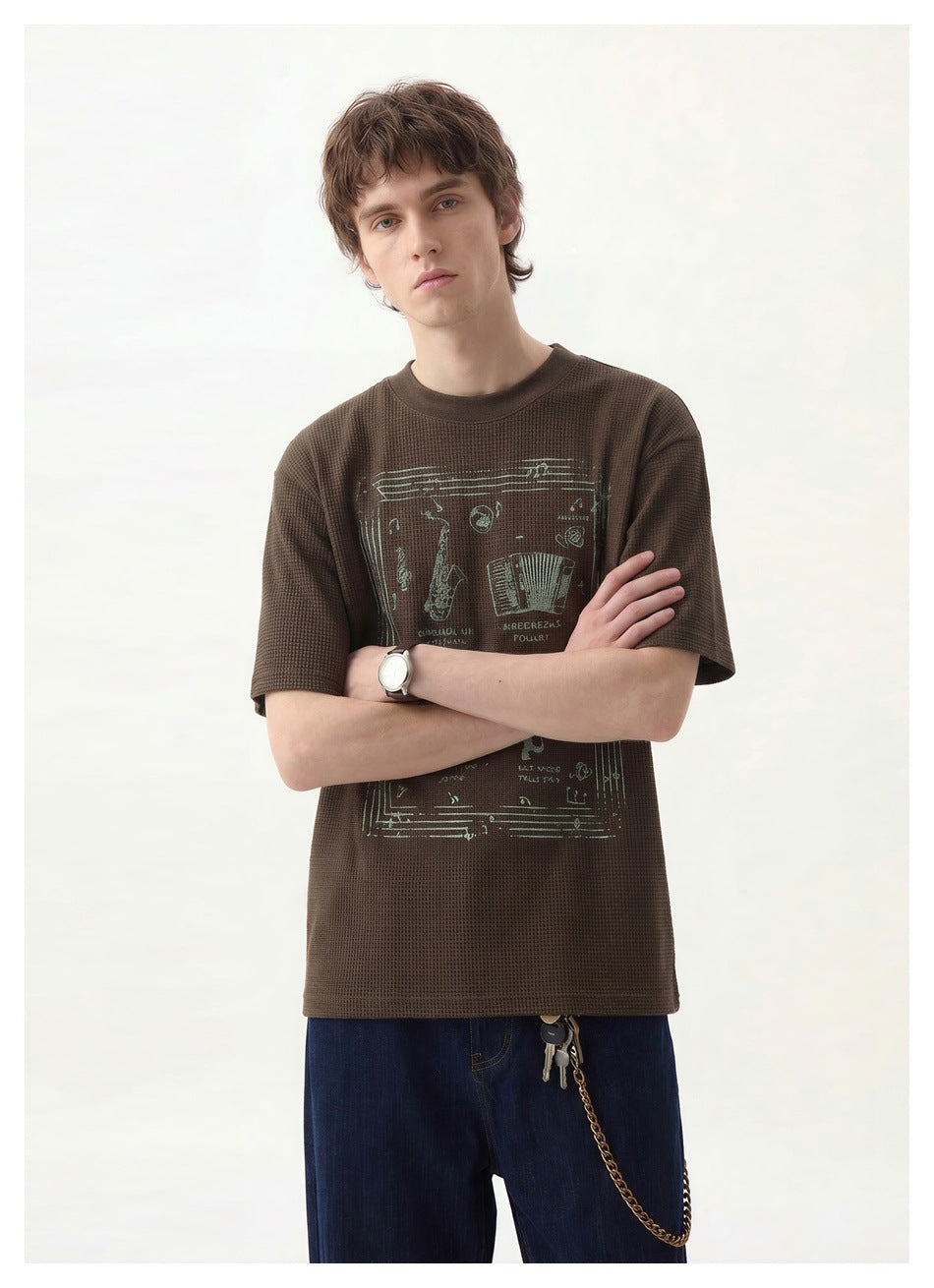 Front view of a model in a dark brown textured T-shirt with a large pale illustrated graphic.