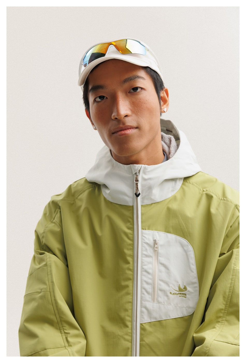 Close-up of a lime-green jacket with a white hood and zippered chest pocket, worn by a man.