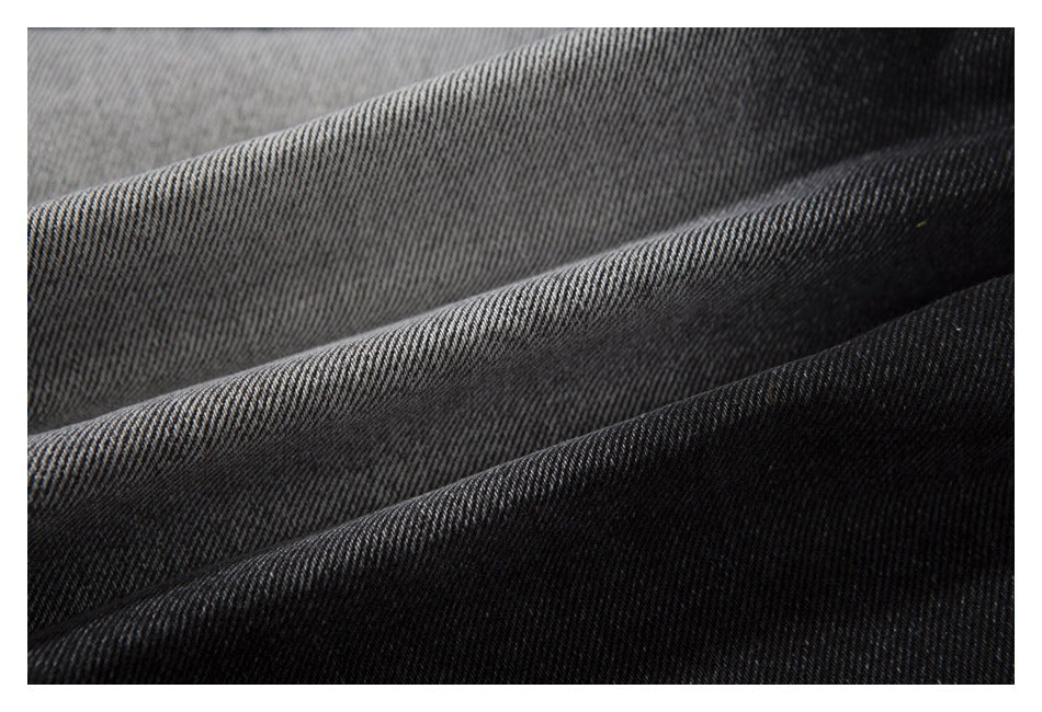 Close-up of folded black-gray denim fabric showing its diagonal weave and faded tones.