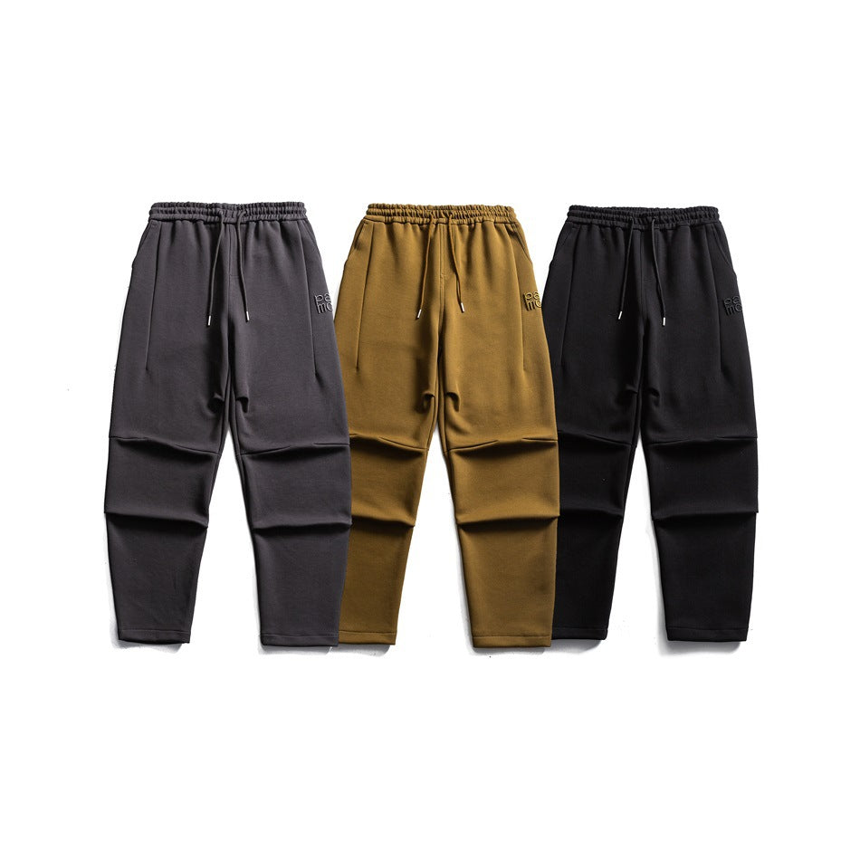 Three pairs of tapered pants laid flat, shown from the front in charcoal, mustard, and black.