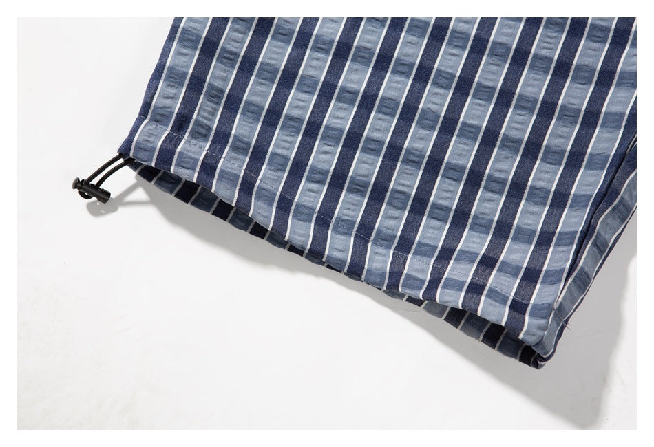 Close-up of the lower hem of blue-gray striped shorts with a black drawcord at the edge.