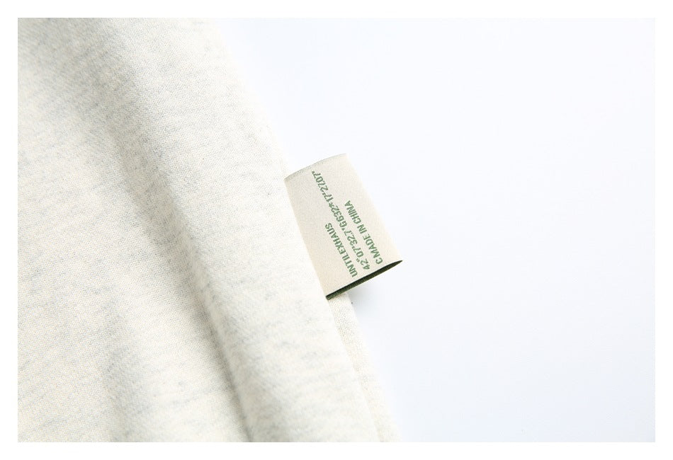 Close-up of a small green-text side label protruding from the off-white sweatshirt fabric.