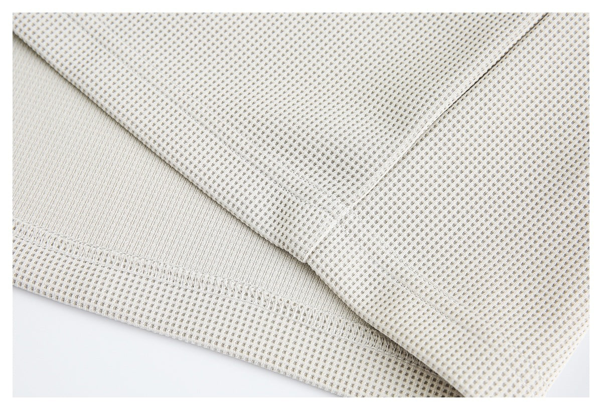 Close-up of the ivory waffle-knit garment's stitched hem and fabric texture.