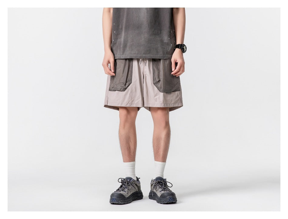 Model wearing light taupe shorts with oversized dark gray front pockets, shown from the front.