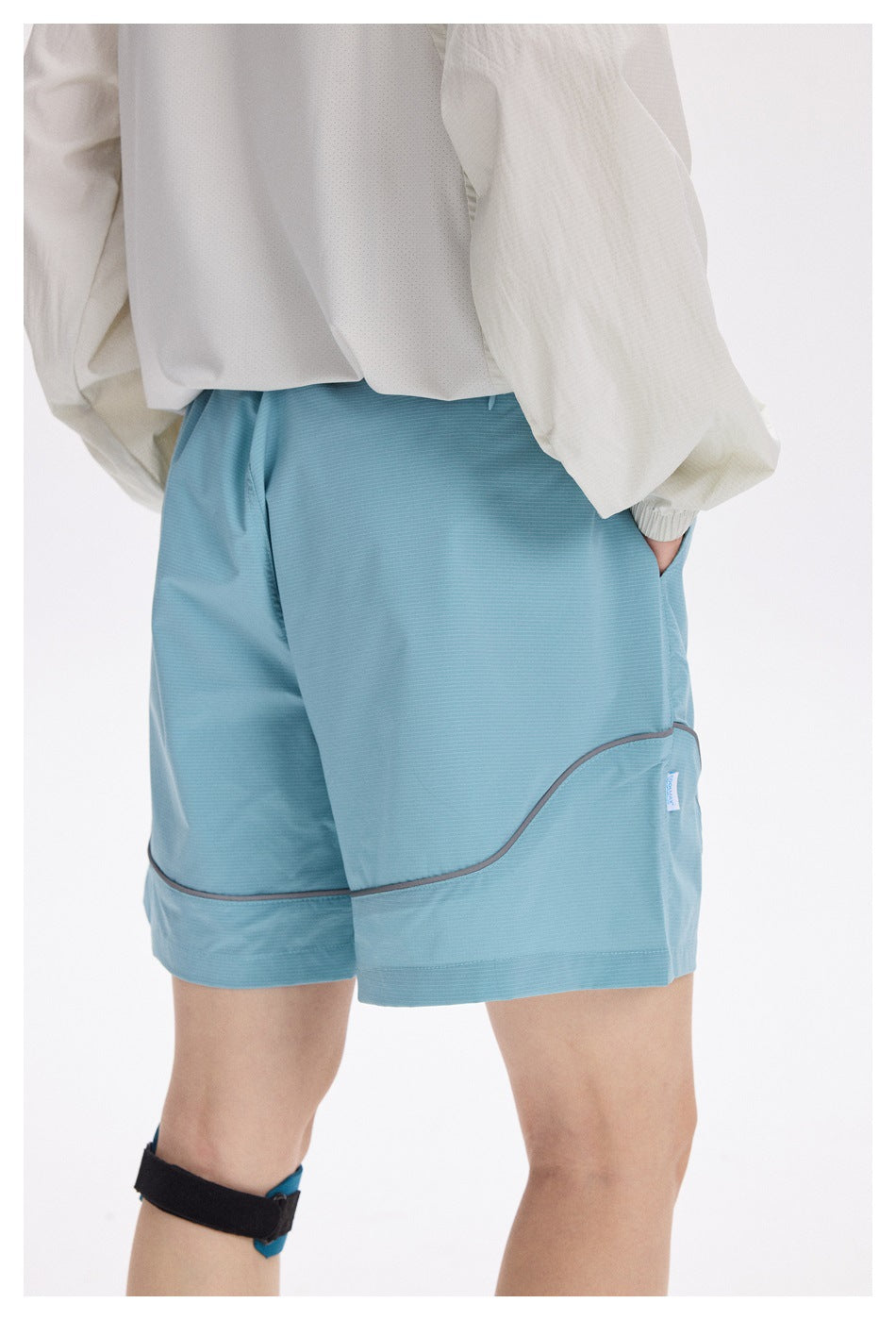 Close rear-side view of light blue shorts with curved gray piping and a side pocket, worn by a person.