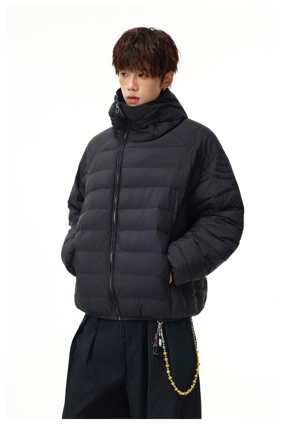 Model wearing a black puffer jacket with a high collar and horizontal quilting, hands in the pockets.