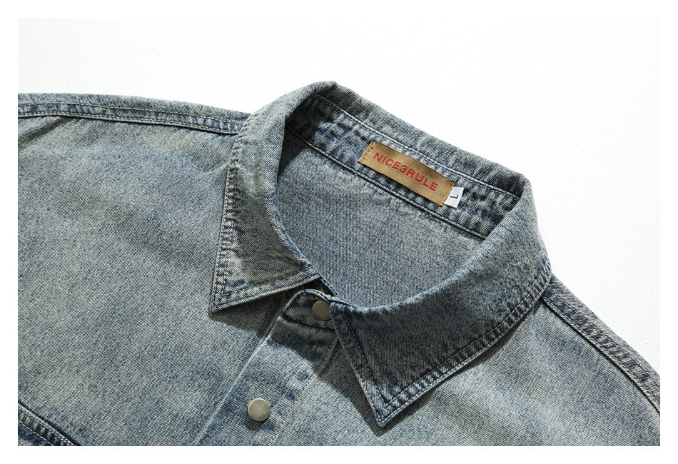 Close-up of a washed blue denim shirt collar, snap button, and sewn-in neck label.