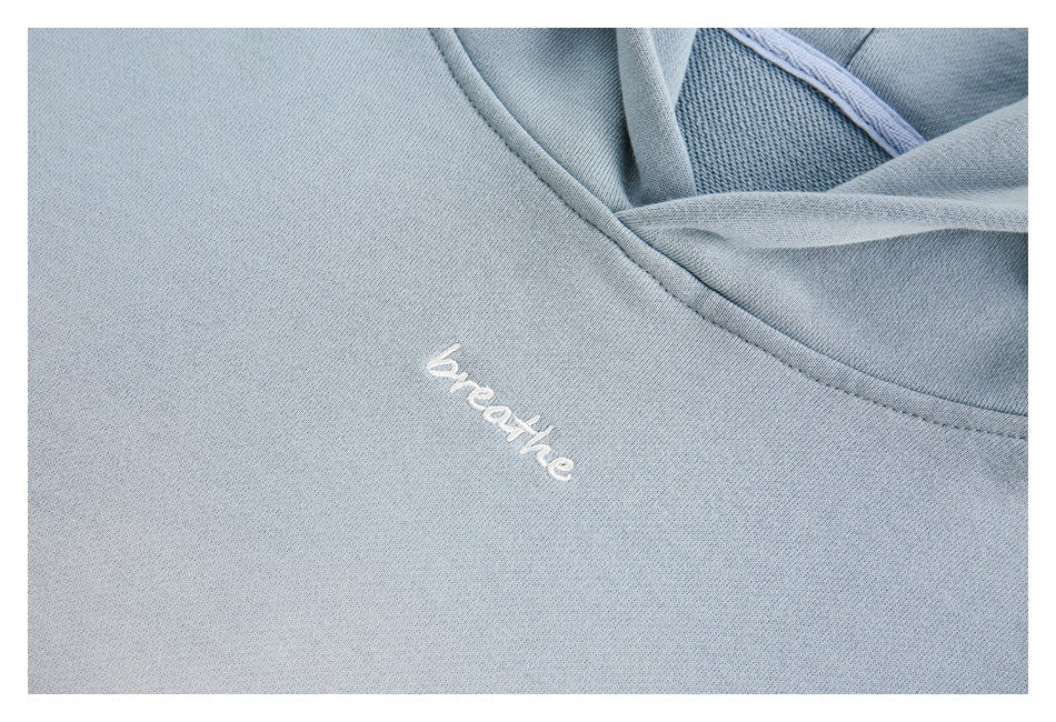 Close-up of white “breathe” embroidery on the chest of a light blue sweatshirt.