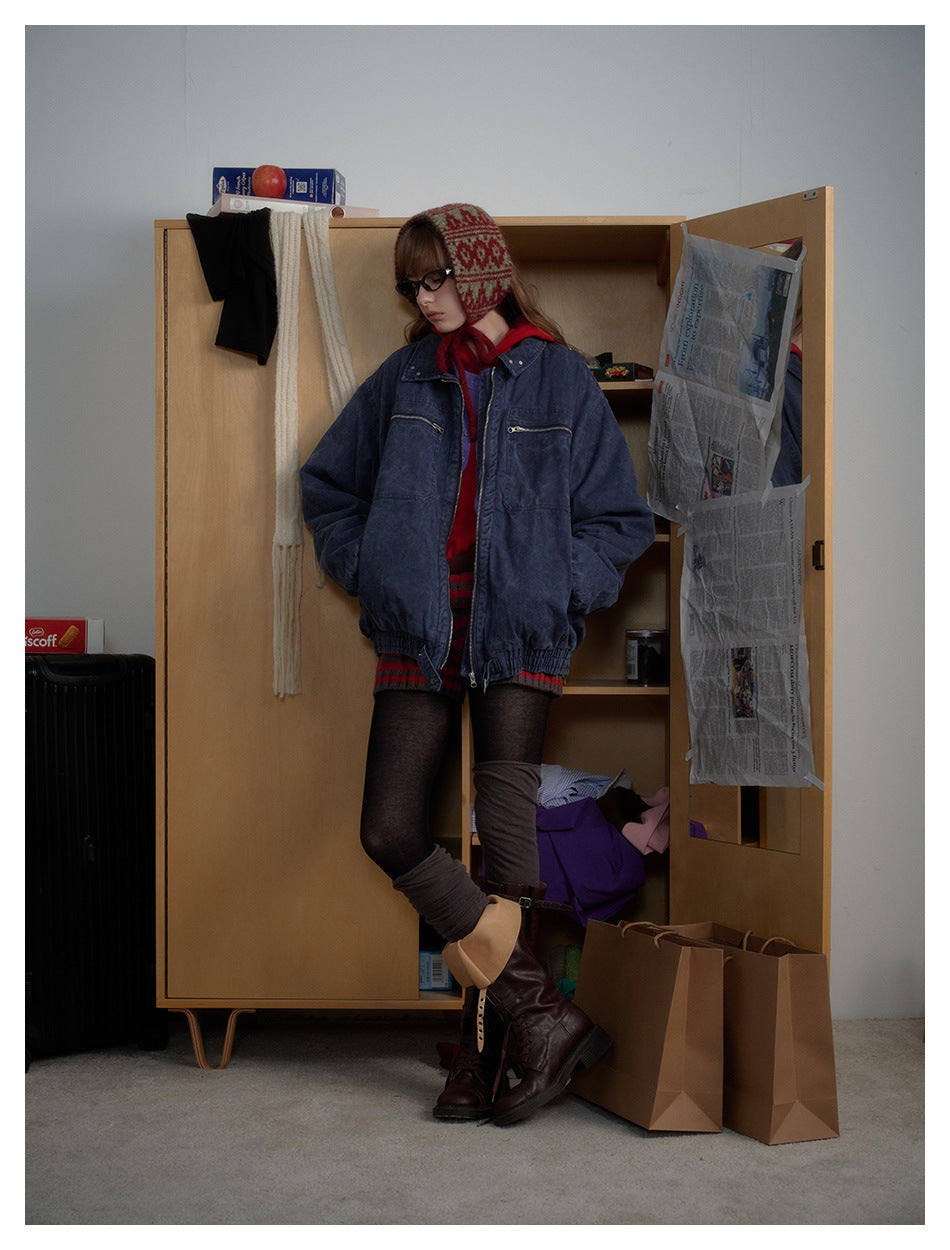 Model in a navy washed zip jacket with chest pockets, leaning against a wooden cabinet, seen from a side angle