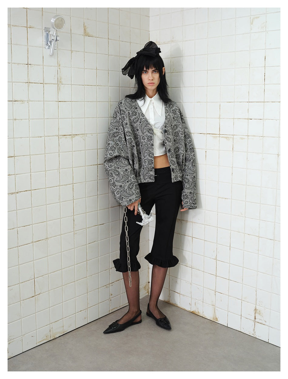 Model wearing an oversized gray paisley button-front jacket with black cropped ruffle-hem pants, shown at a slight angle.