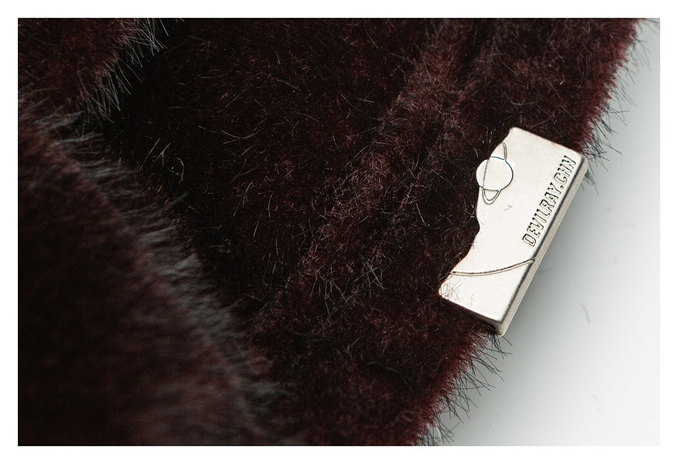 Close-up of a small metal brand plaque attached to dark burgundy plush fabric.