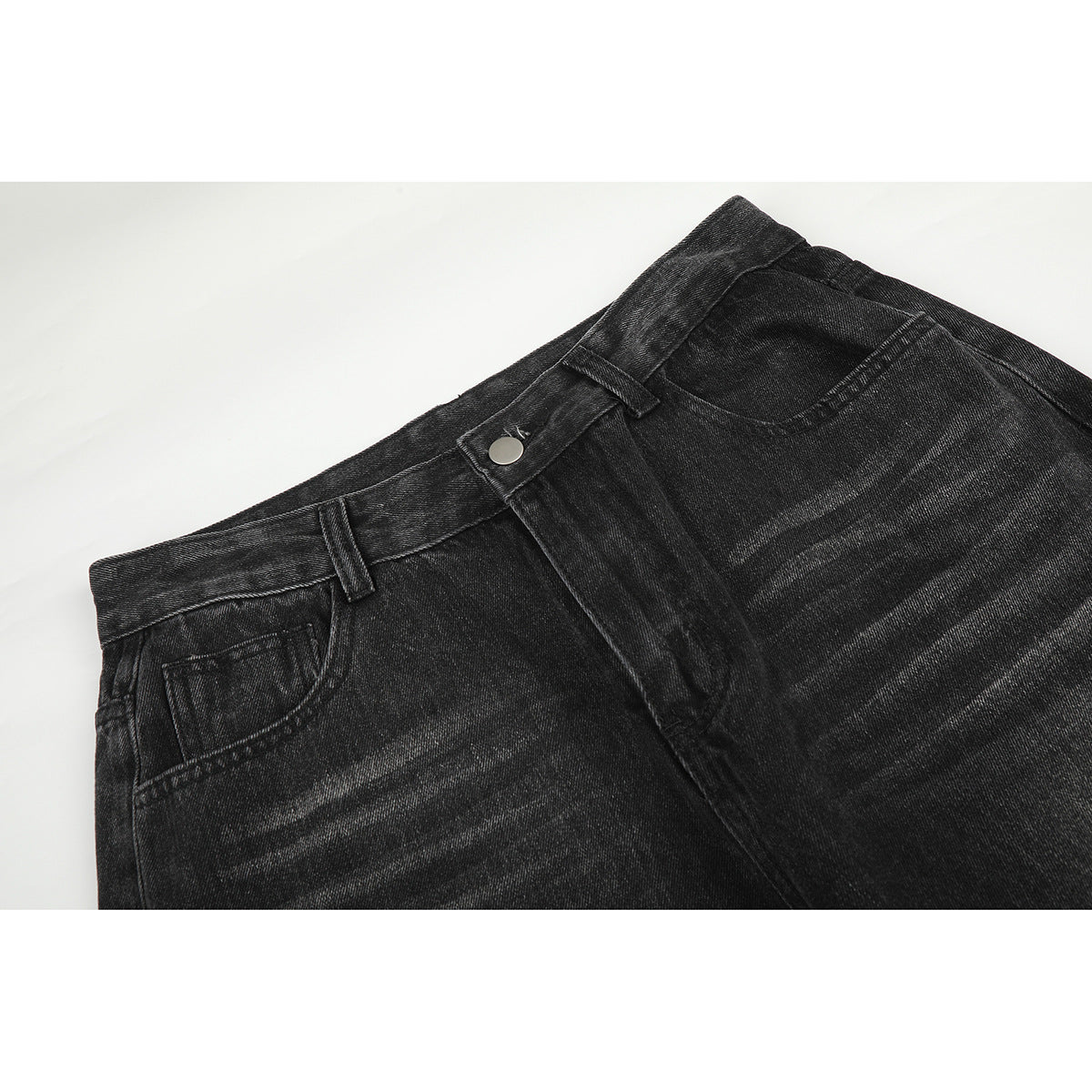 Close-up of charcoal-black jeans showing the front waistband, button, belt loops, pockets and faded whiskering.