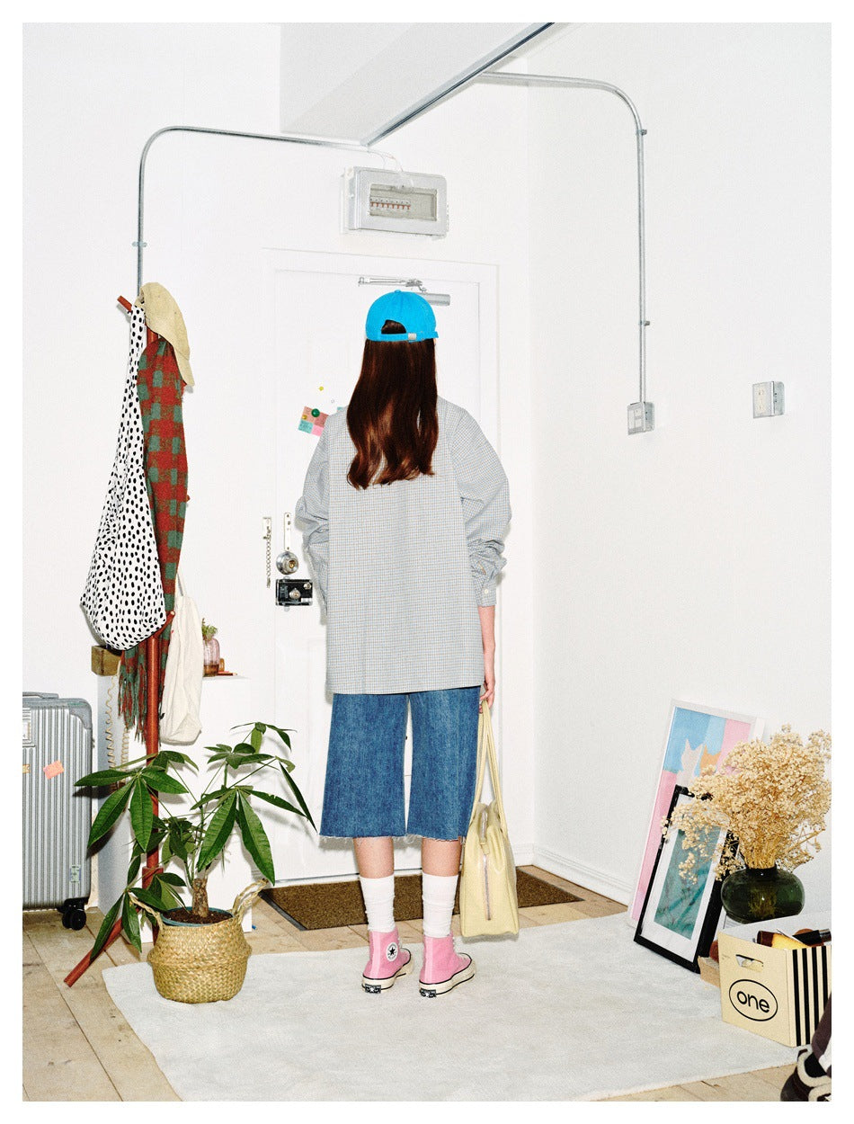 Back view of a model in a pale blue check button-up shirt and denim shorts, wearing a blue cap and pink shoes.