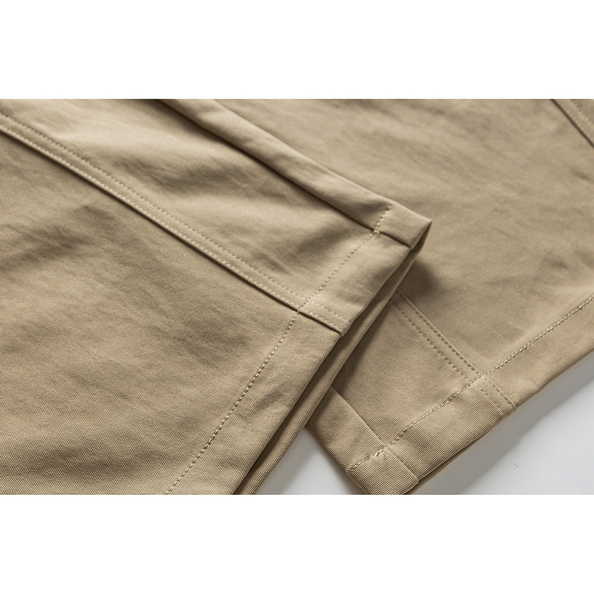Close-up of taupe trouser fabric and stitched hem with a folded cuff.