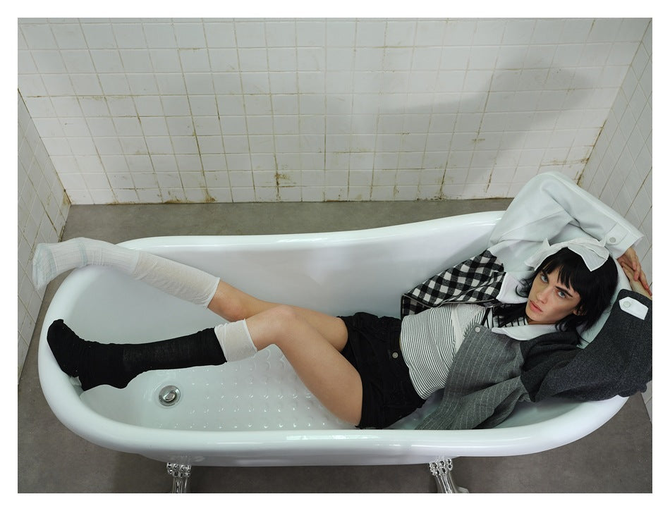 Model lying back in a bathtub in the colorblock jacket with a striped top, black shorts and socks