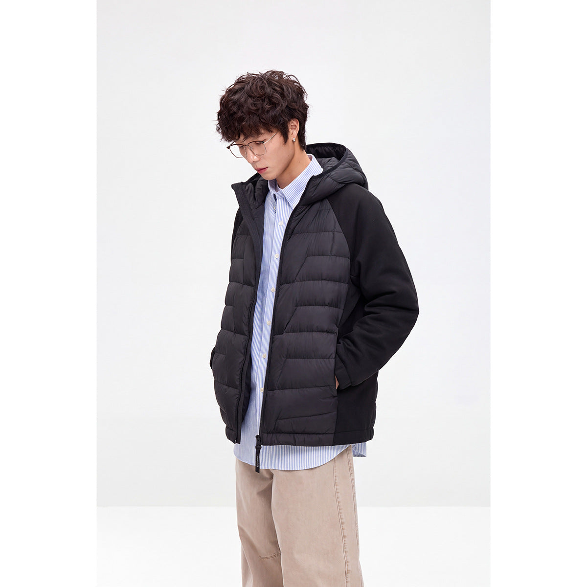 Model wearing a black hooded jacket with horizontal quilted front panels and solid sleeves, shown at an angle.