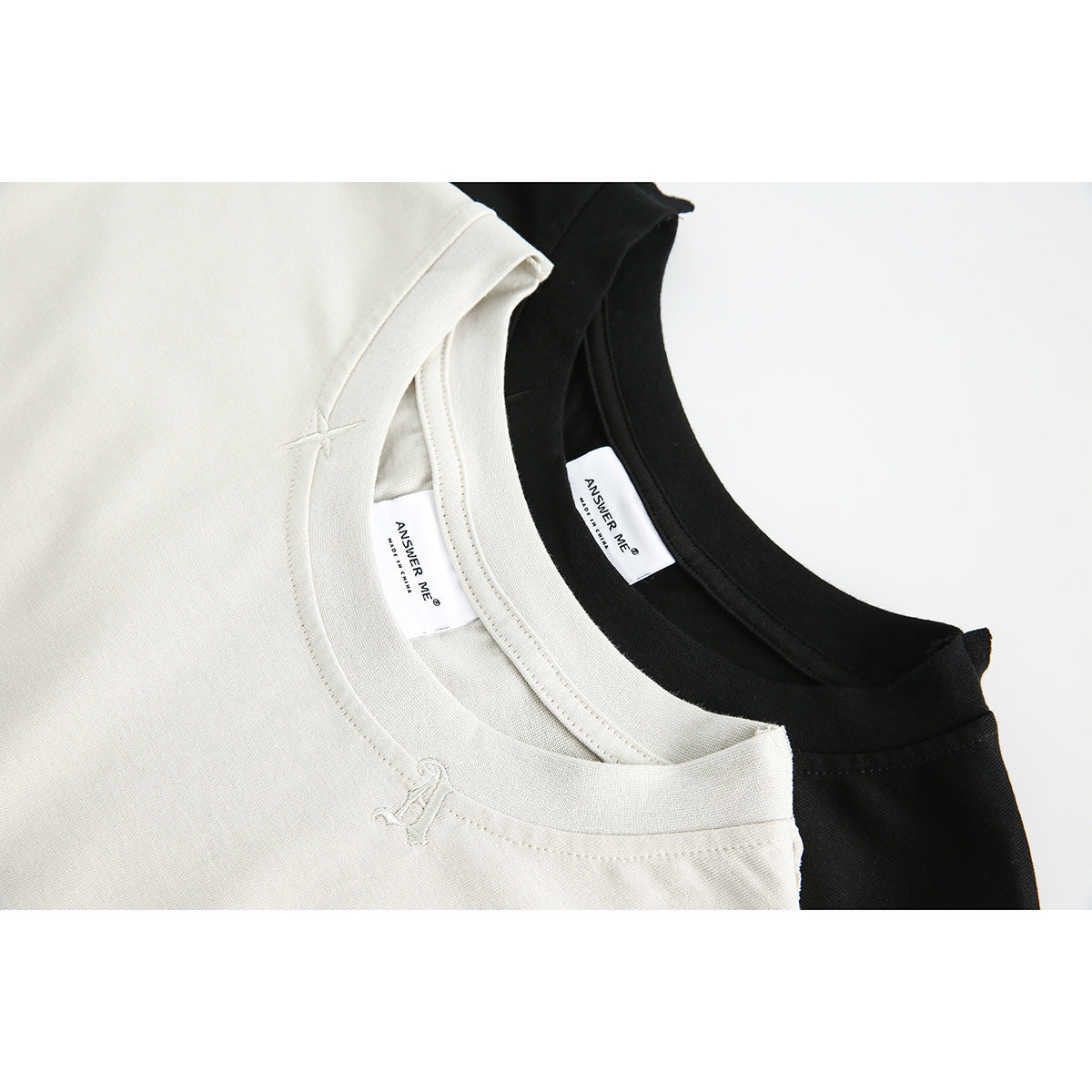 Close-up of cream and black sleeveless tops showing crew necks, inner labels and small stitched accents.