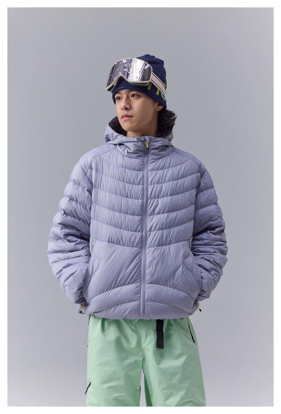 Front view of a model wearing a lavender hooded quilted jacket and mint-green ski pants.