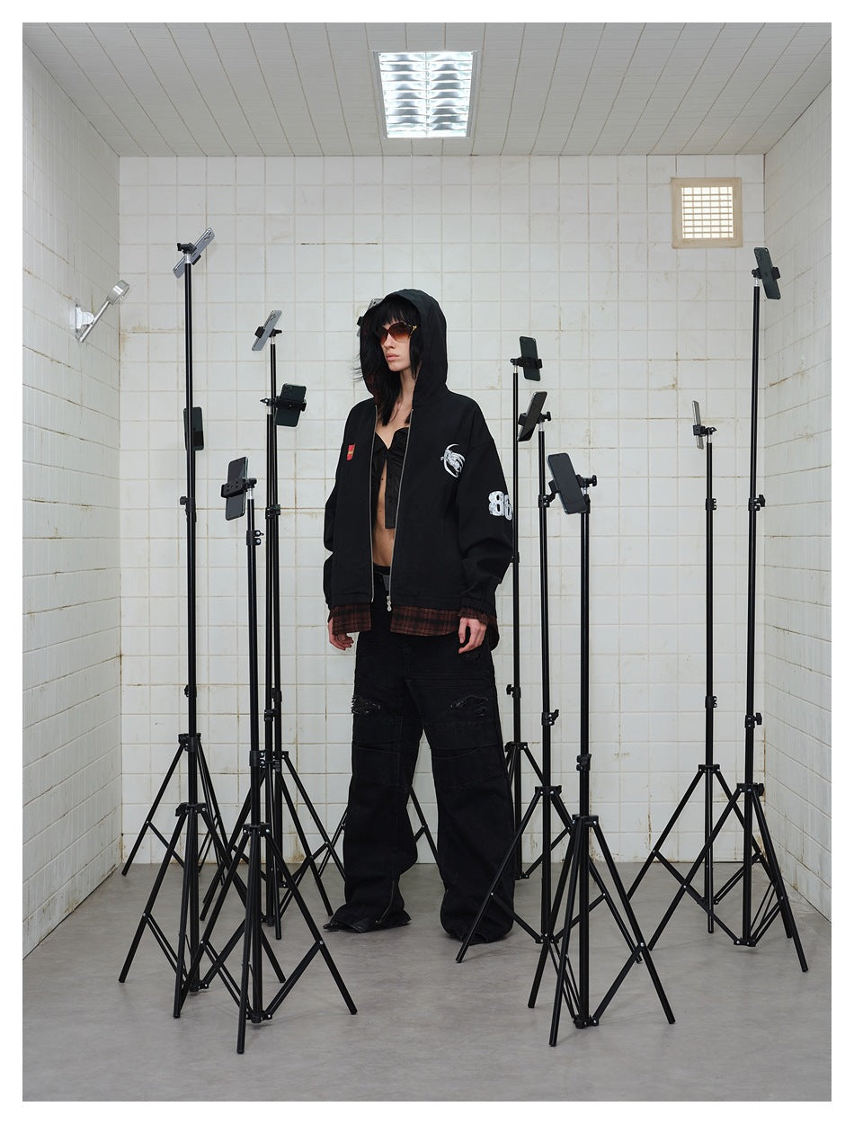 Model in a black hooded jacket with plaid hem and cuffs, white moon graphic and sleeve number, standing in a tiled room