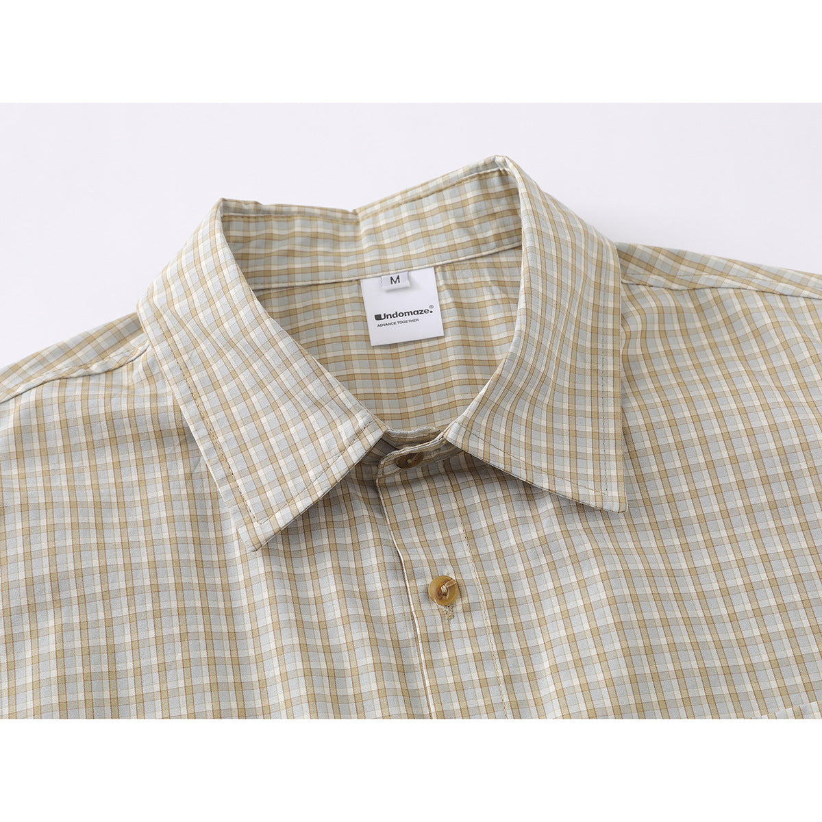 Close-up of a cream button-up shirt with a tan and gray windowpane check, pointed collar, and visible neck label.