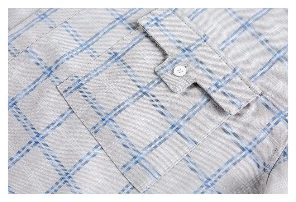 Close-up of a buttoned chest pocket on a gray shirt with a blue plaid pattern.