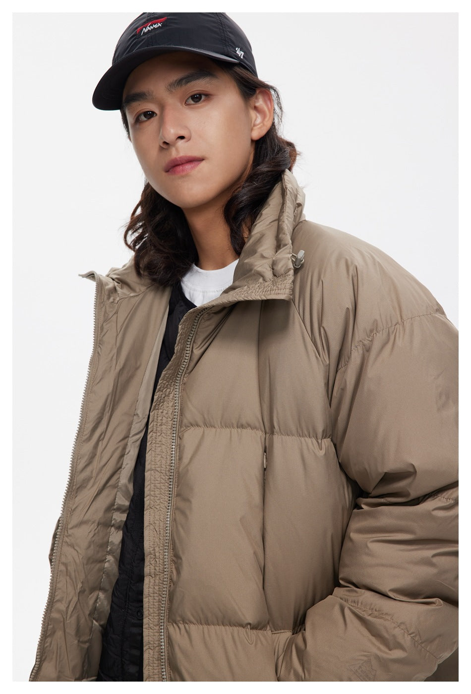 Close view of a model wearing a taupe puffer jacket, showing its quilted panels, high collar, and open front.