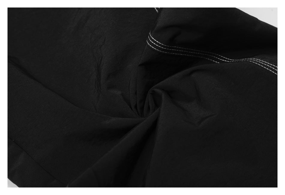 Close-up of black trouser fabric gathered around a seam with white contrast stitching.