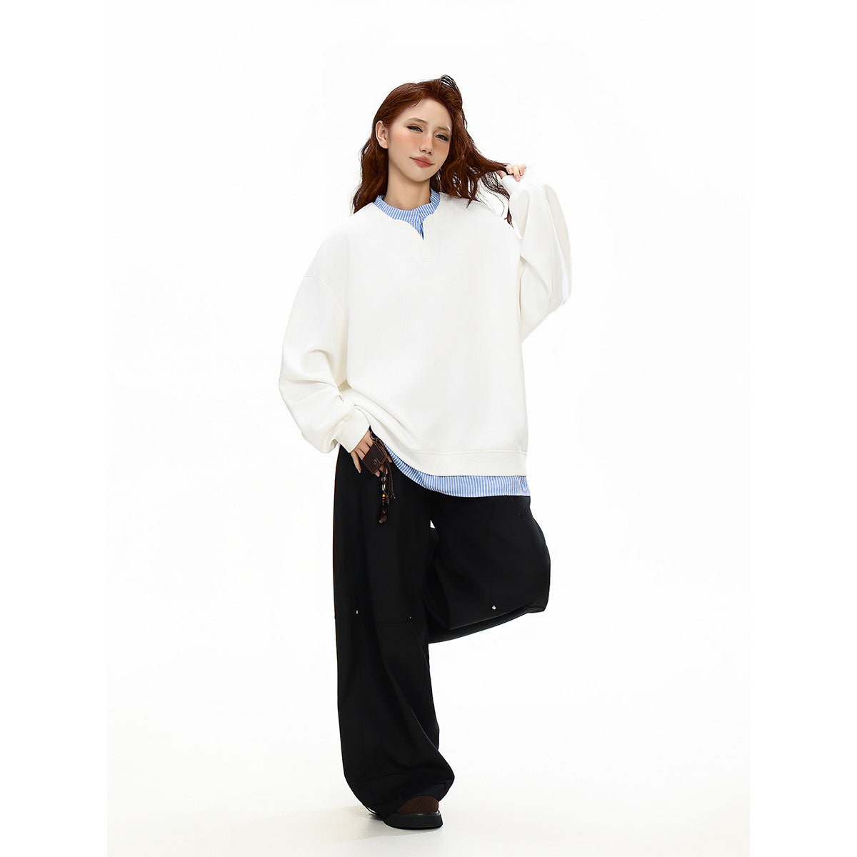 Model wearing an oversized white sweatshirt over a blue-and-white striped shirt, shown from the front.