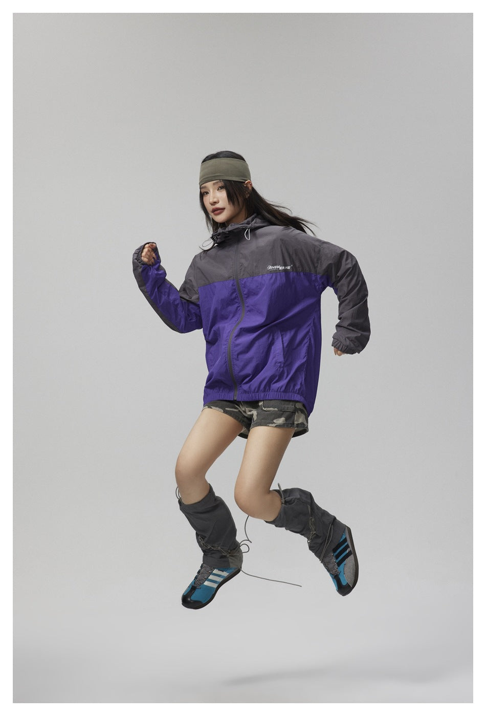 Model wearing a zipped purple and charcoal hooded jacket with camouflage shorts and dark leg warmers.