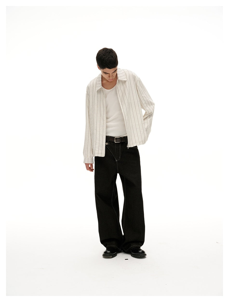 Model looks down while wearing an open cream striped shirt over a white tank with black trousers.