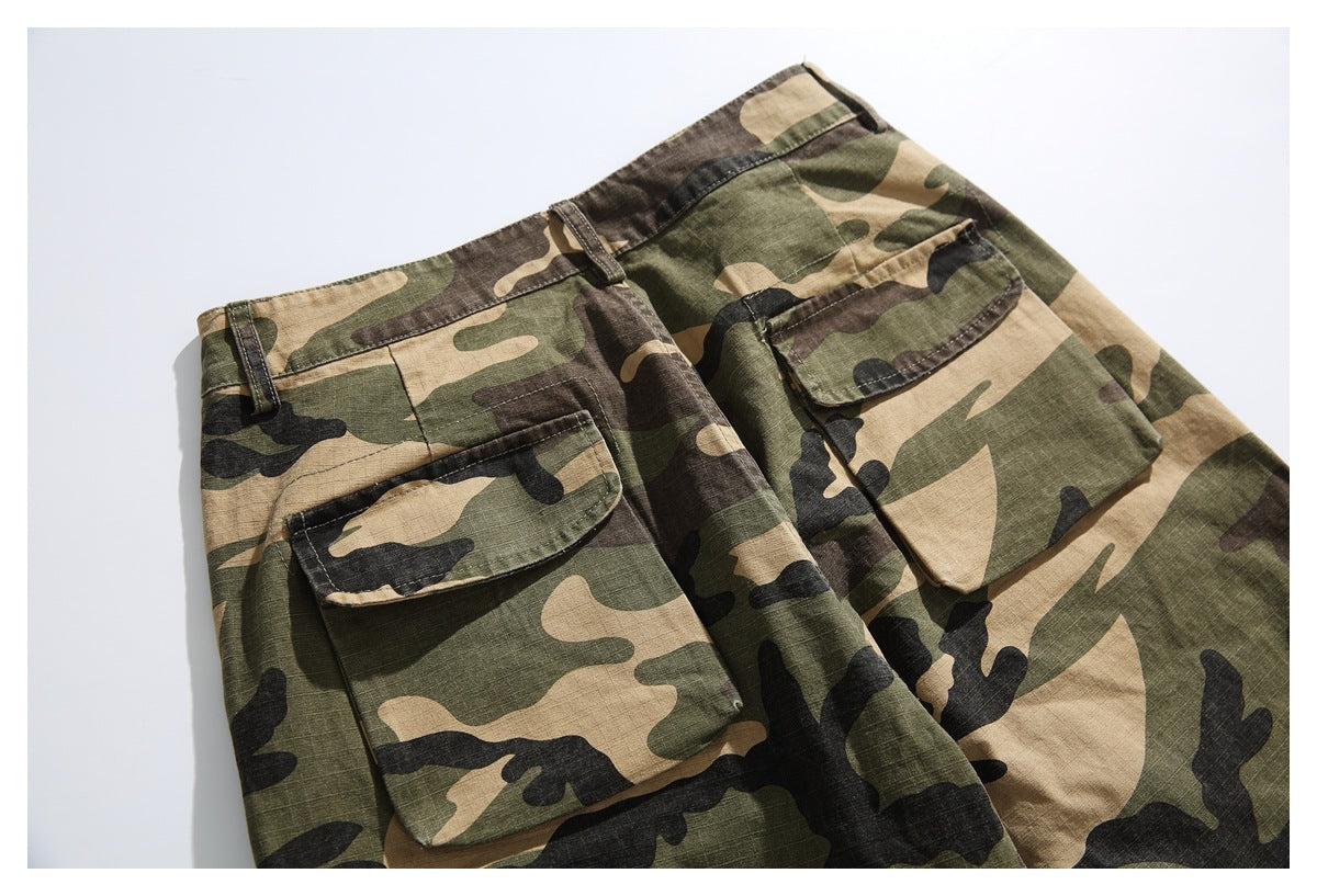 Flat lay of camouflage trousers showing the waistband, belt loops, and two large flap pockets.
