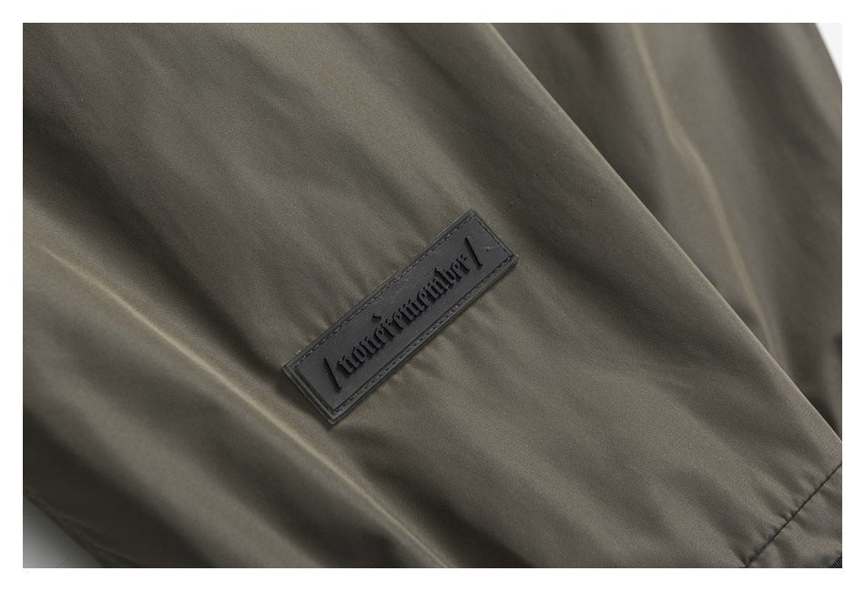Close-up of a dark rectangular brand patch on gray-olive garment fabric.
