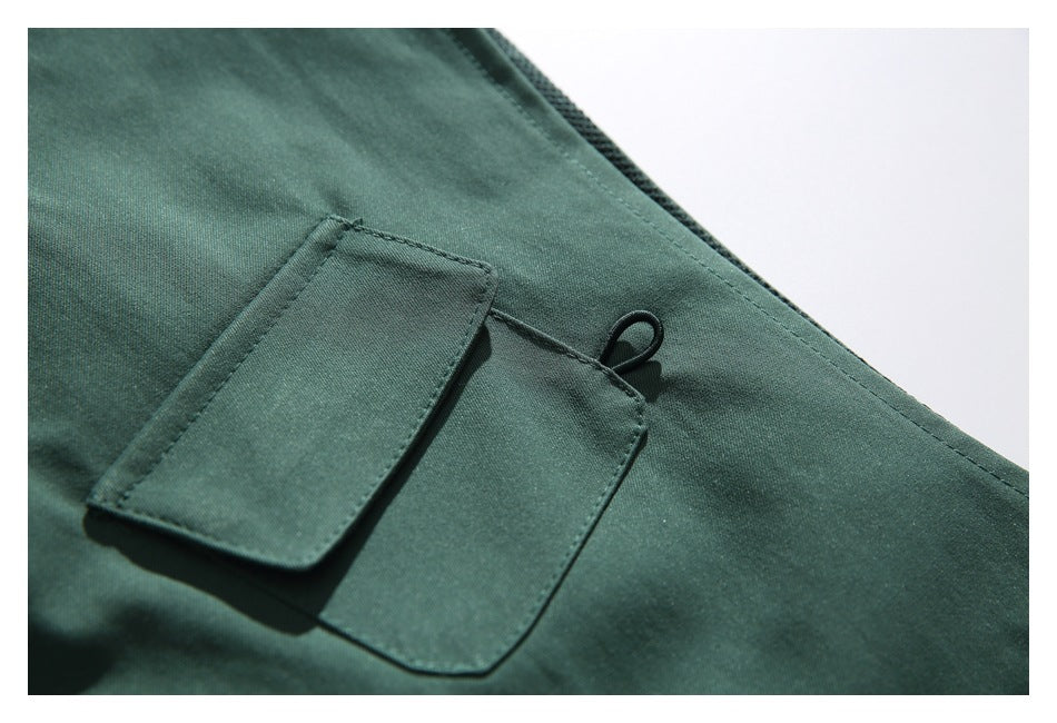 Close-up of a dark green garment's rectangular flap pocket and small loop.