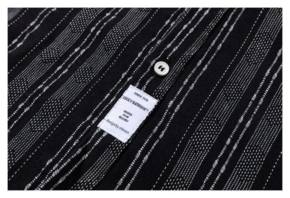 Close-up of black fabric with irregular white dashed stripes, a white button, and a sewn-in brand label.