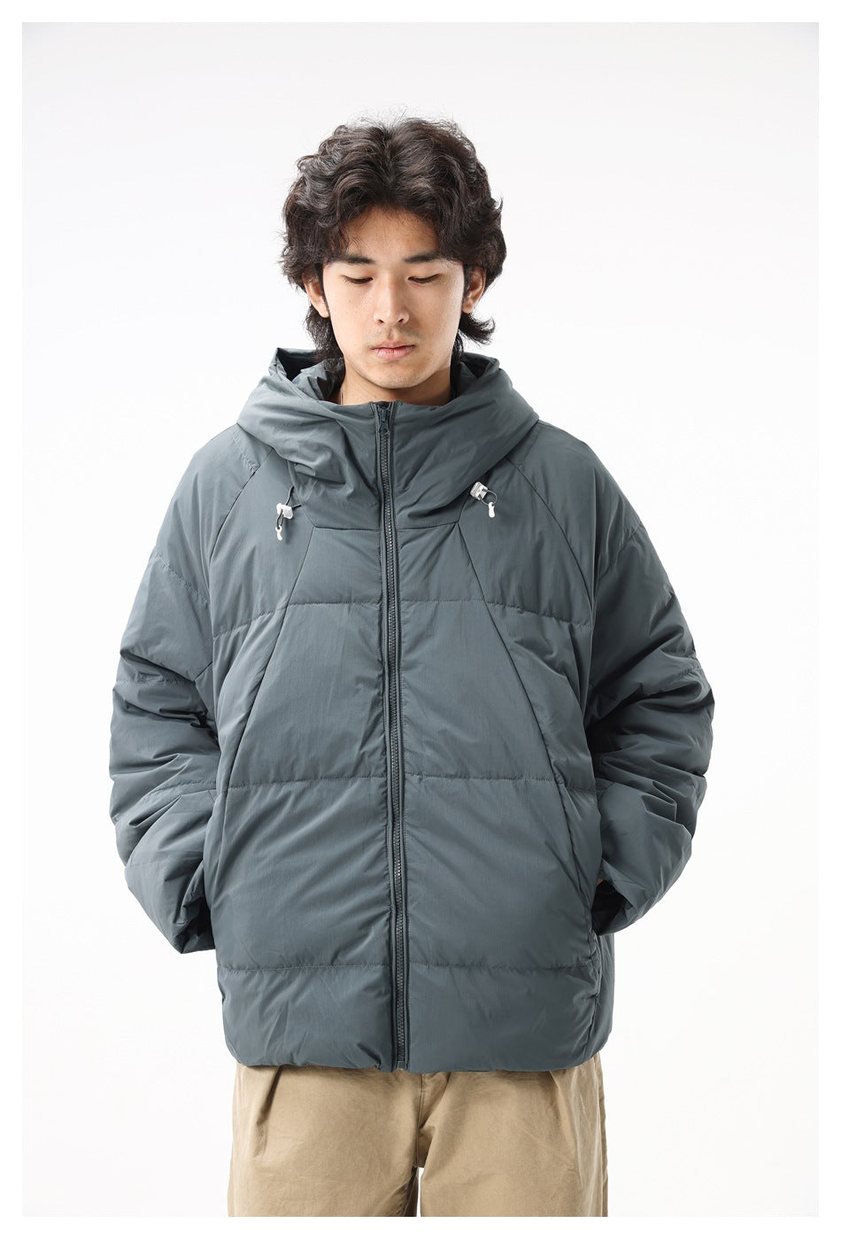 Model wearing a slate gray hooded puffer jacket, shown from the front with the zipper and chest drawcords visible.