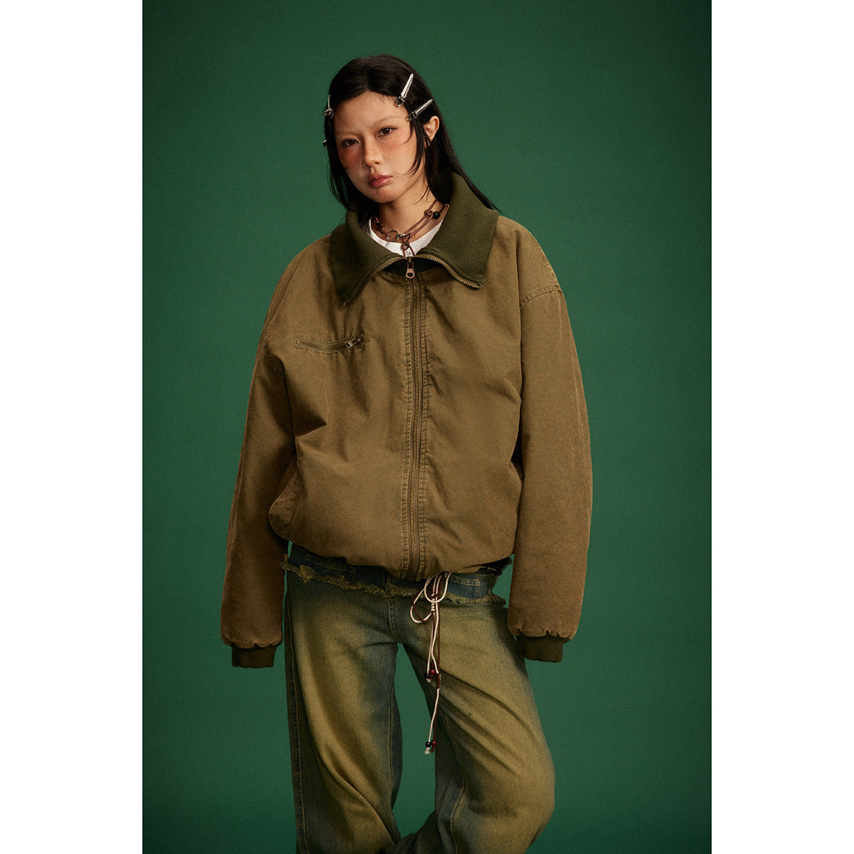 Front view of a model in a brown zip jacket with a dark wide collar, chest zipper pocket, and elastic cuffs.