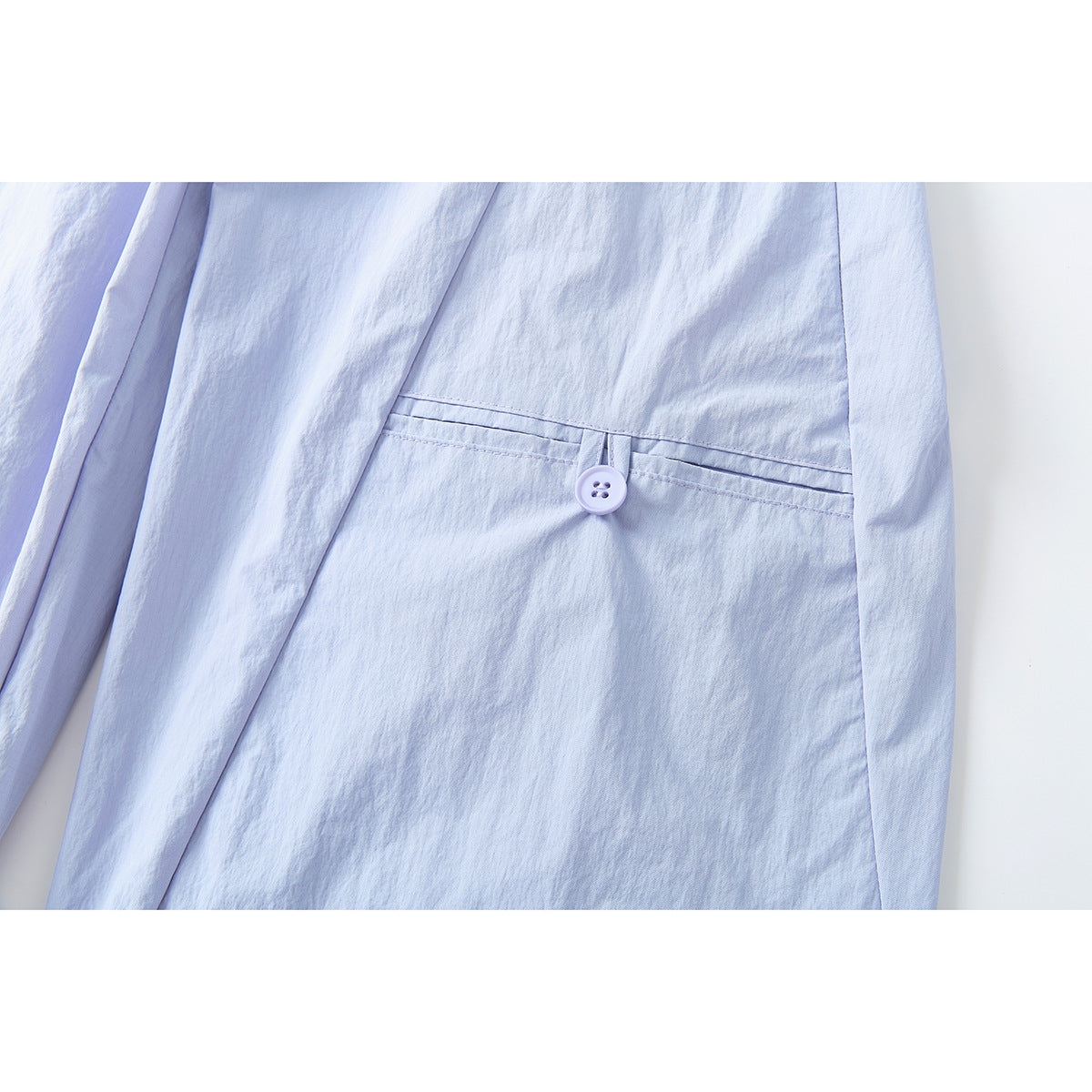 Close-up of pale lavender pants showing a narrow buttoned welt pocket and surrounding seams.