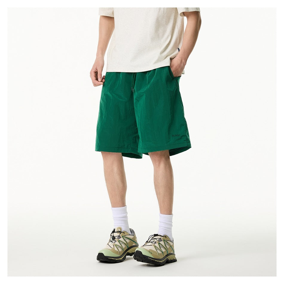 Cropped model wearing emerald green drawstring shorts, shown from the front with a light T-shirt and trail shoes.