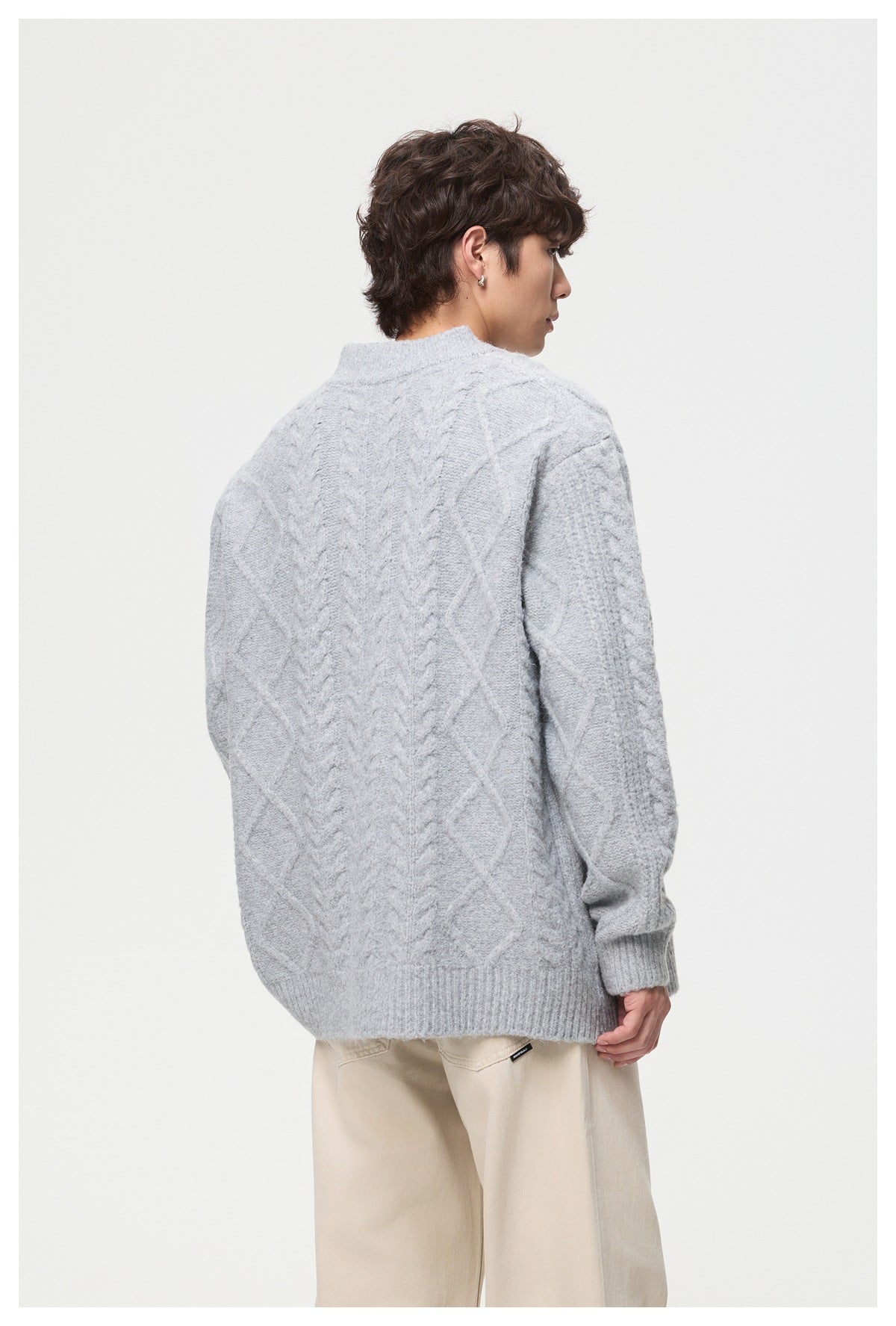 Rear view of a model wearing a light gray cable-knit cardigan with ribbed cuffs and hem.