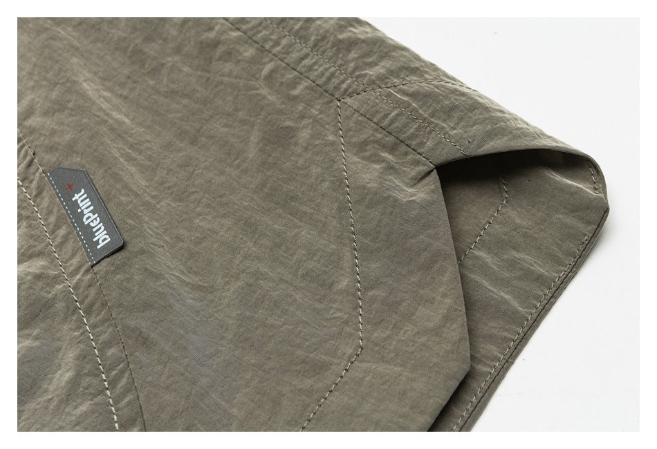 Close-up of a stitched pocket area and sewn Blueprint+ label on the gray-green shorts.