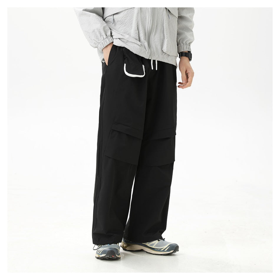 Model wearing black wide-leg pants with pleated knee panels and clipped pouch, with a light gray jacket and sneakers