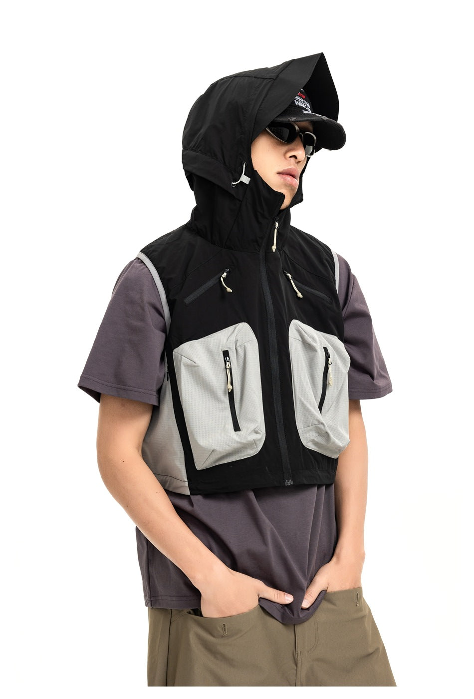 Front view of a model wearing a black hooded vest with two large pale gray zip pockets over a purple T-shirt.
